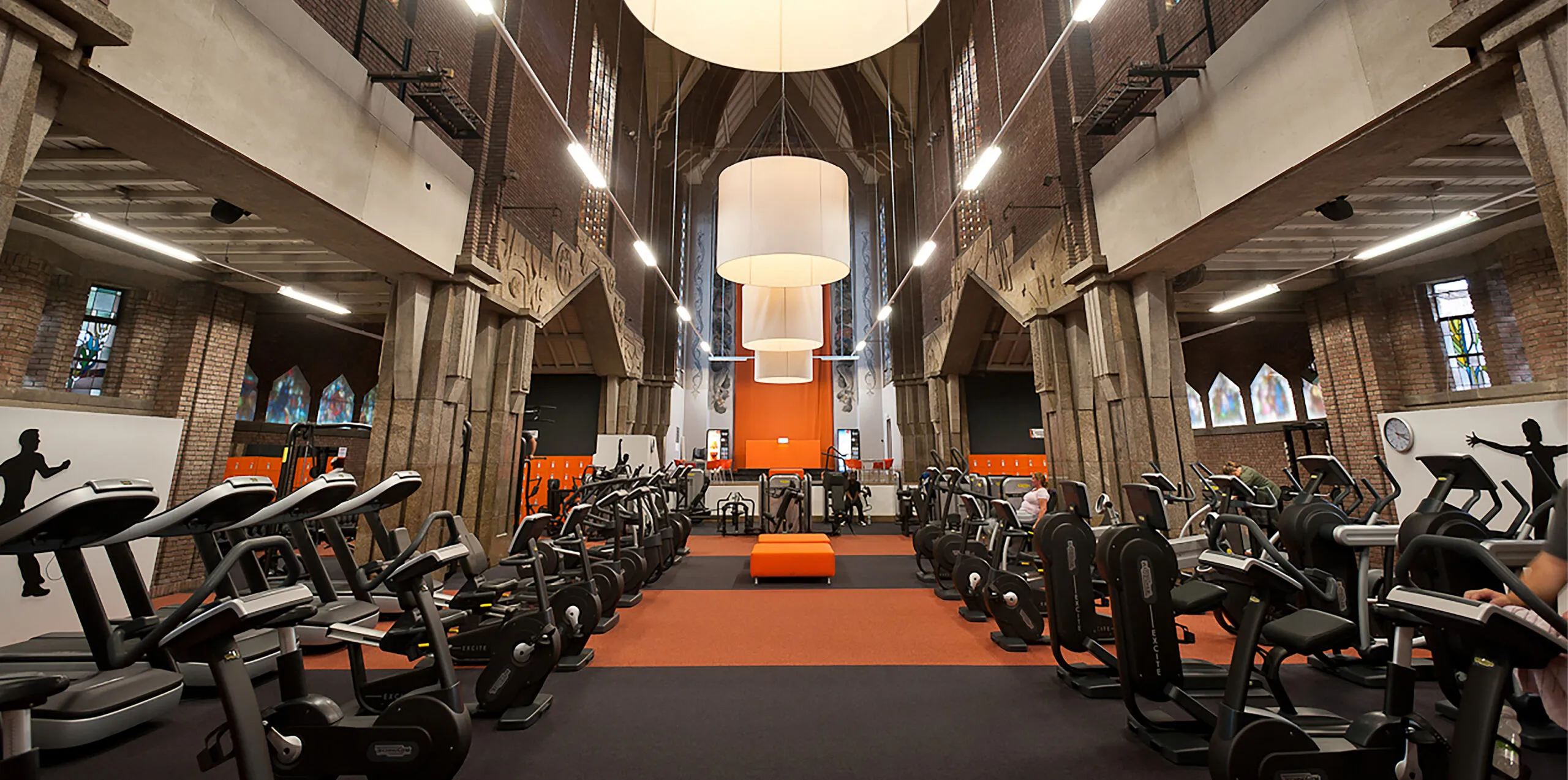 BASIC-FIT club in een voormalige kerk in Maastricht, met cardiotoestellen tussen de gemetselde zuilen en de glas-in-loodramen. Locatiefotografie door Fitbrand.