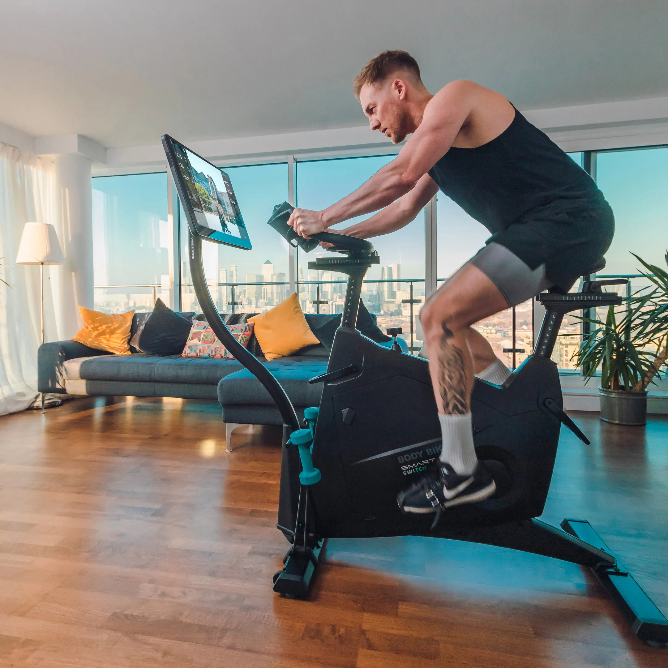 Man bedient het draaibare touchscreen van de Body Bike SMART+ SWITCH in een appartement met uitzicht over Londen. Fotografie door Fitbrand.