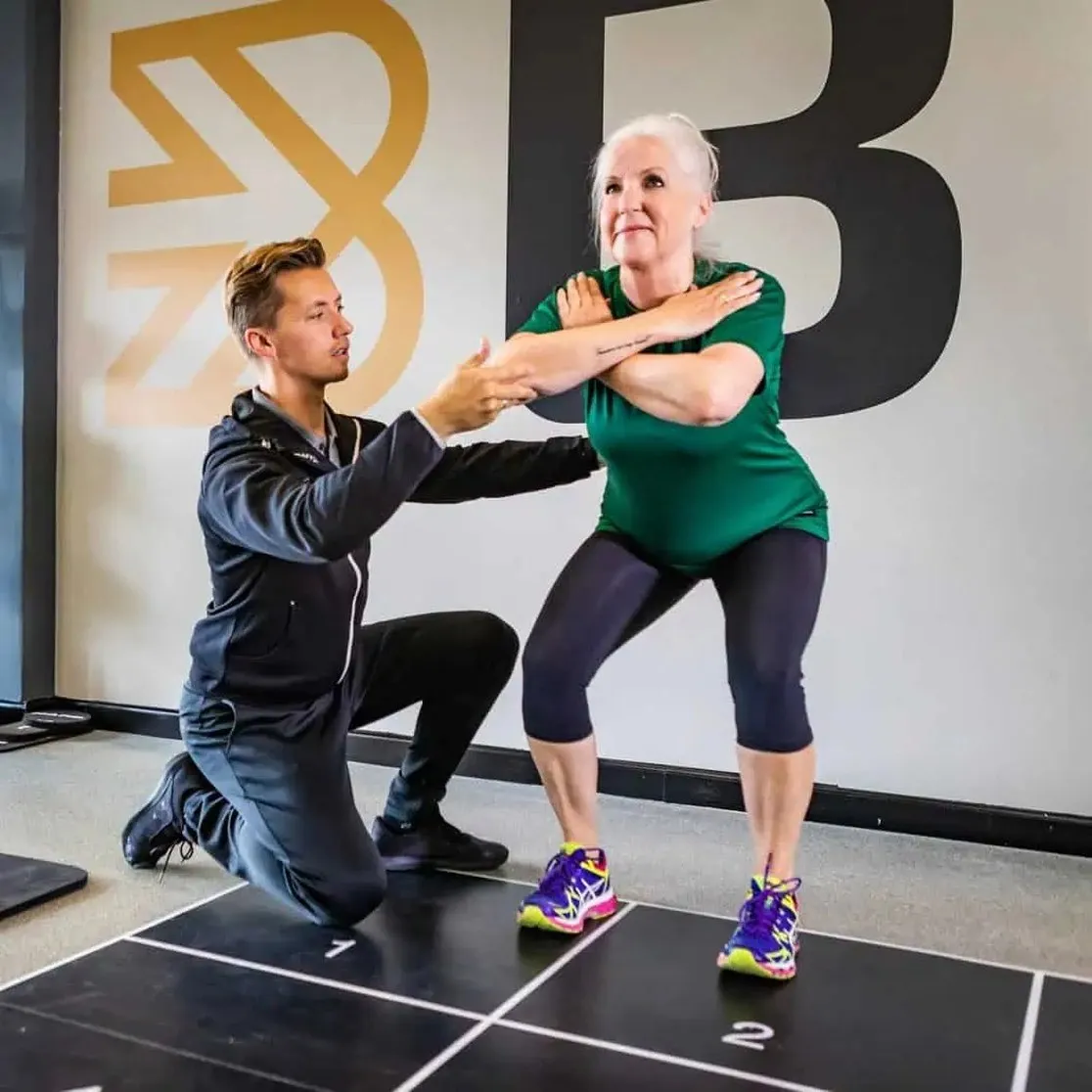 Oudere cliënt oefent een squat met haar personal trainer van BeneFIT Studio. Fotografie door Fitbrand