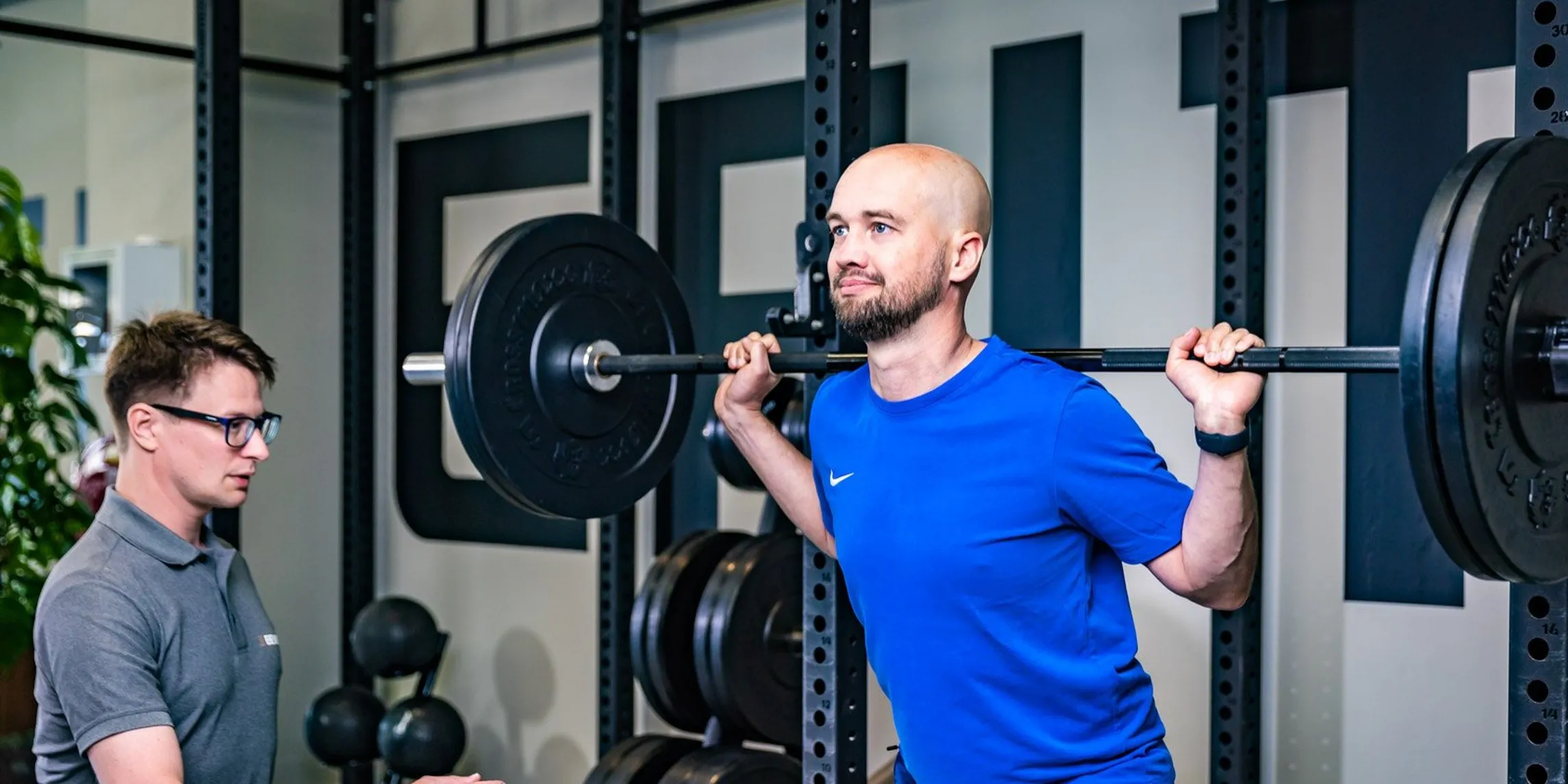Cliënt doet een squat met halter onder toezicht van een personal trainer van BeneFIT Studio. Fotografie door Fitbrand