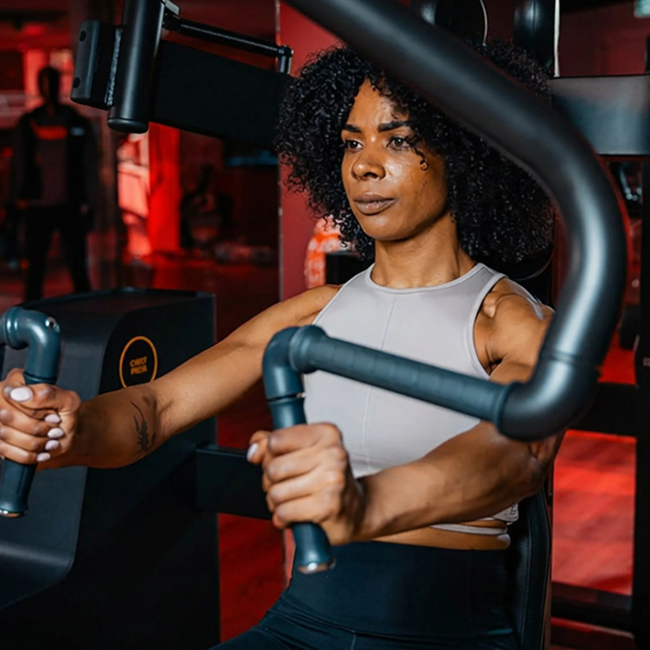 Vrouw lacht op de chestpress in de rood verlichte gym van TwelveX