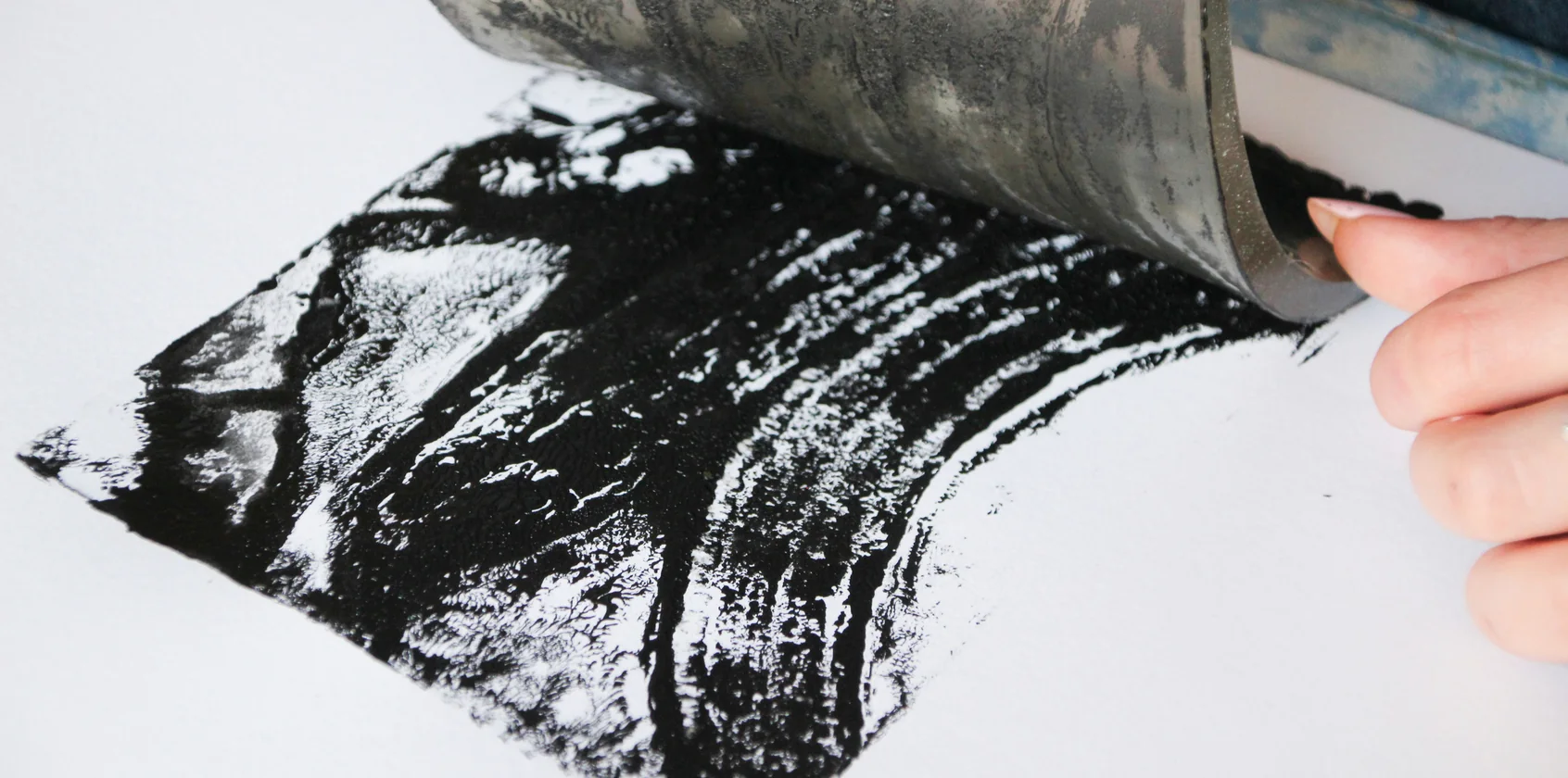 Een hand rolt zwarte inkt over wit papier met een drukroller
